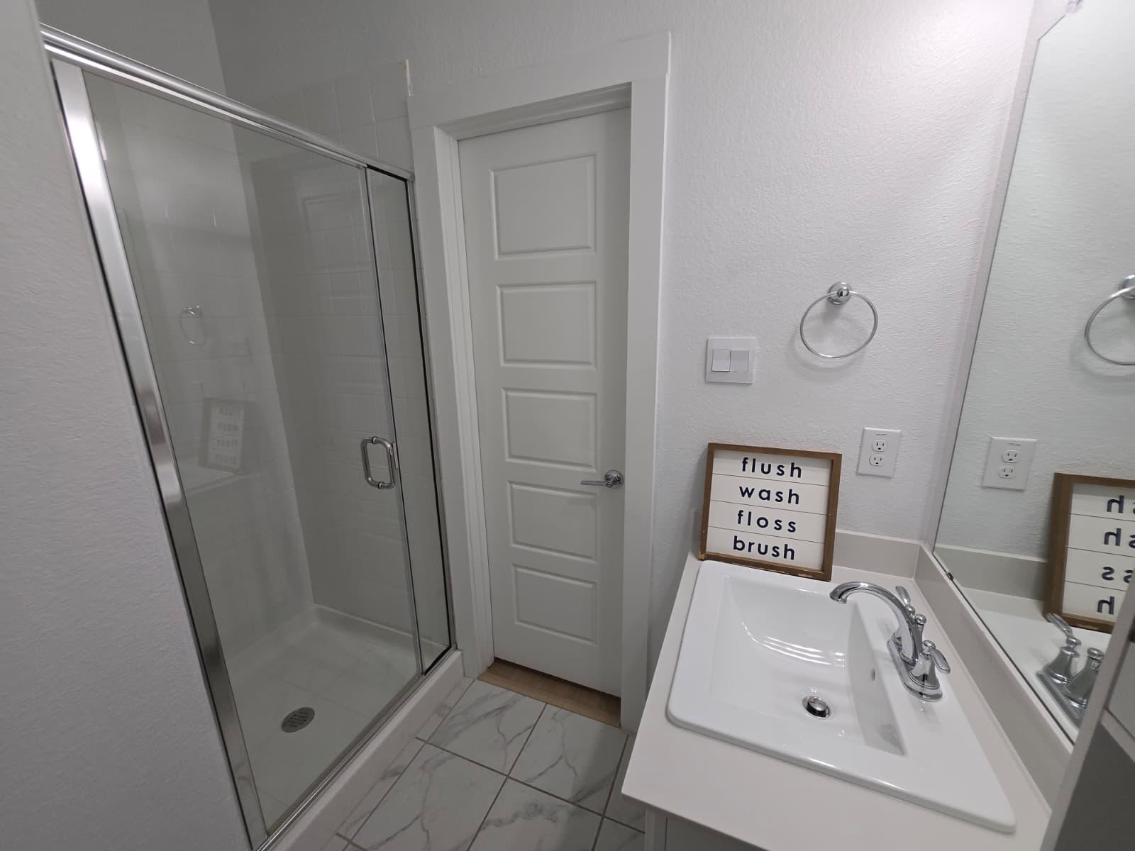 Bathroom with a glass-enclosed step-in shower, white sink vanity, mirror and towel ring