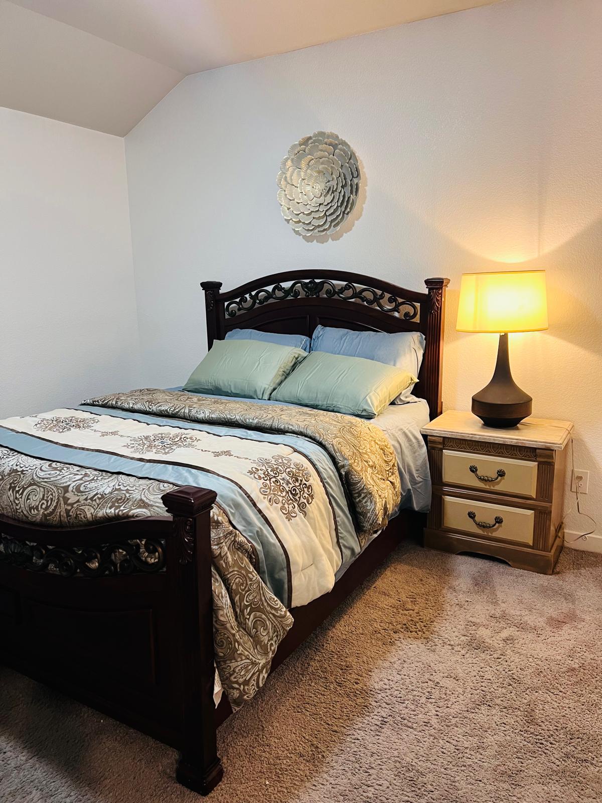 Bedroom with a dark wood bed frame, layered bedding, a nightstand and a lit table lamp