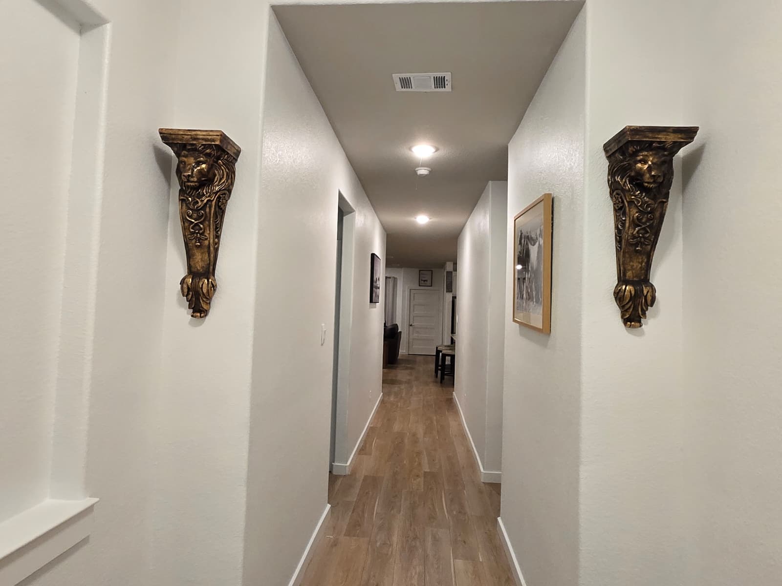 Hallway with white walls, decorative carved wall sconces, framed artwork and wood-look flooring