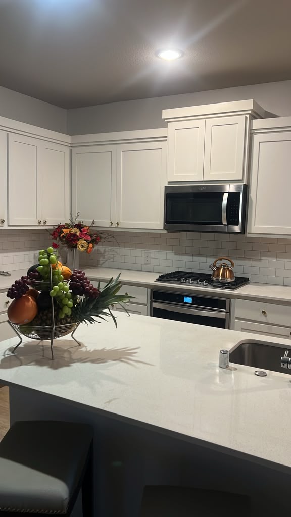 Kitchen island with a white countertop, a fruit basket, white cabinets, a microwave and a gas cooktop