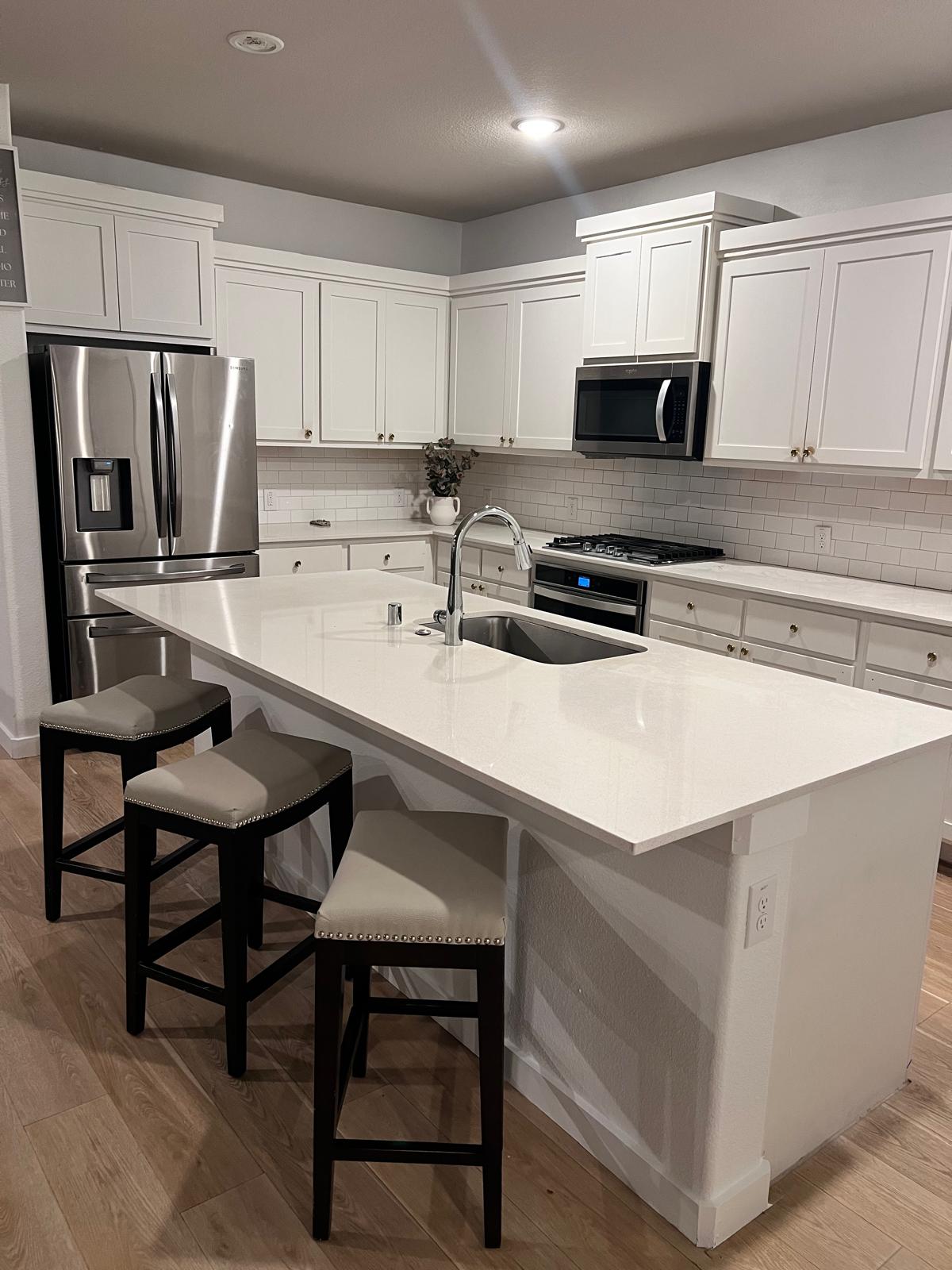 Kitchen with white cabinets, stainless steel appliances, a quartz island and three bar stools